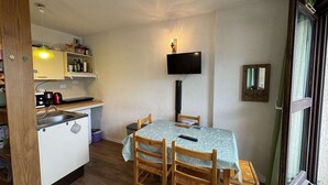 A compact kitchen with a dining area, a TV mounted on the wall, and a window with curtains. - Studio for 4 in Serre-Chevalier, Southeast Balcony (Saint-Chaffrey)