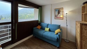 A room with a blue sofa, a wooden cabinet, a floor lamp, and a poster on the wall. - Studio for 4 in Serre-Chevalier, Southeast Balcony (Saint-Chaffrey)