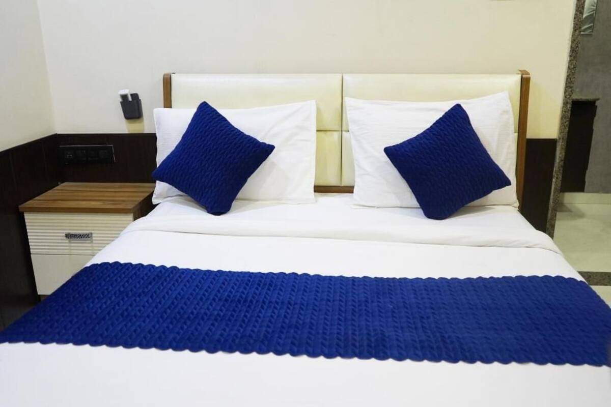 Ein Bett mit weißer Bettwäsche und zwei blauen Kissen, ein Nachttisch aus Holz mit Schublade sowie ein an der Wand befestigtes Telefon.
