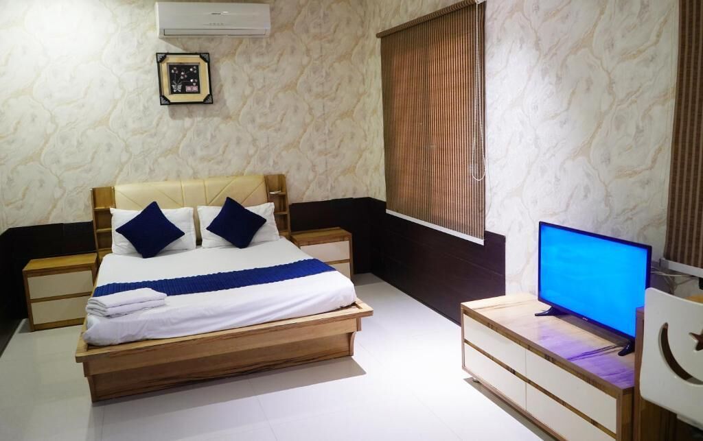 A bedroom with a bed, bedside tables, a television, and a window with blinds.