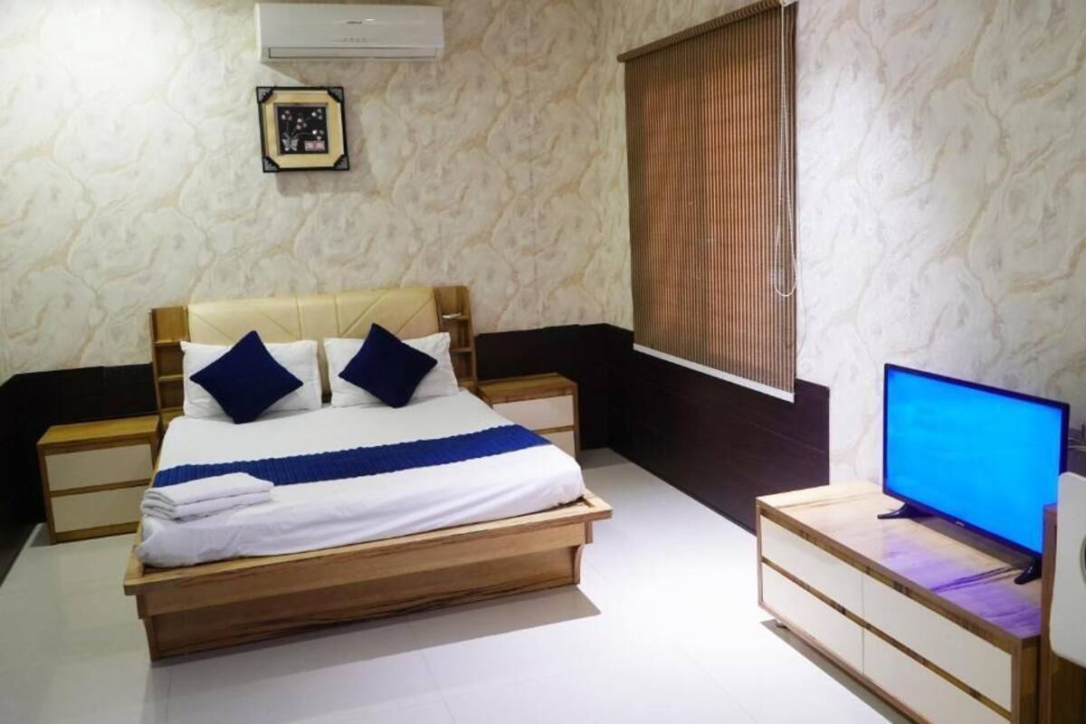 Ein Schlafzimmer mit einem Bett, Nachttischen, einem Fernseher und einem Fenster mit Jalousien.