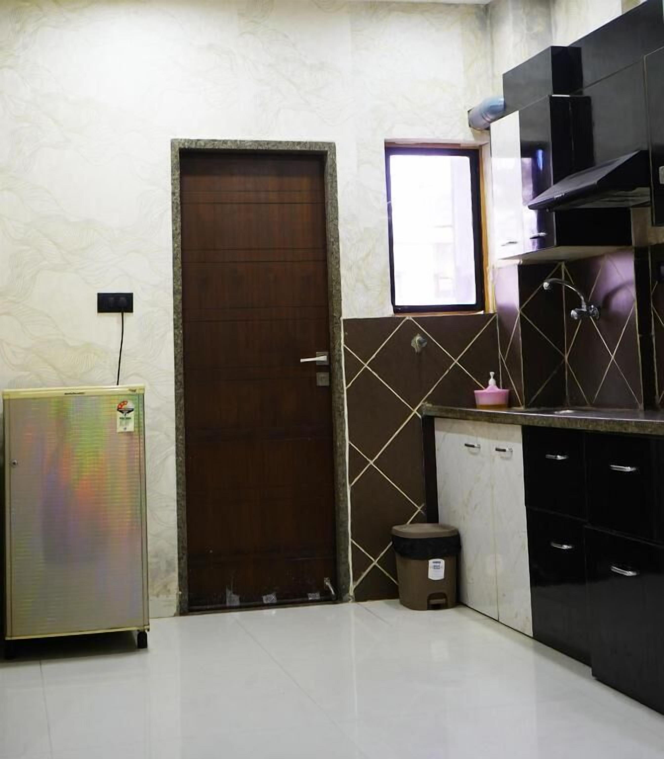 Una cocina compacta con refrigerador, puerta de madera, ventana y lavamanos.