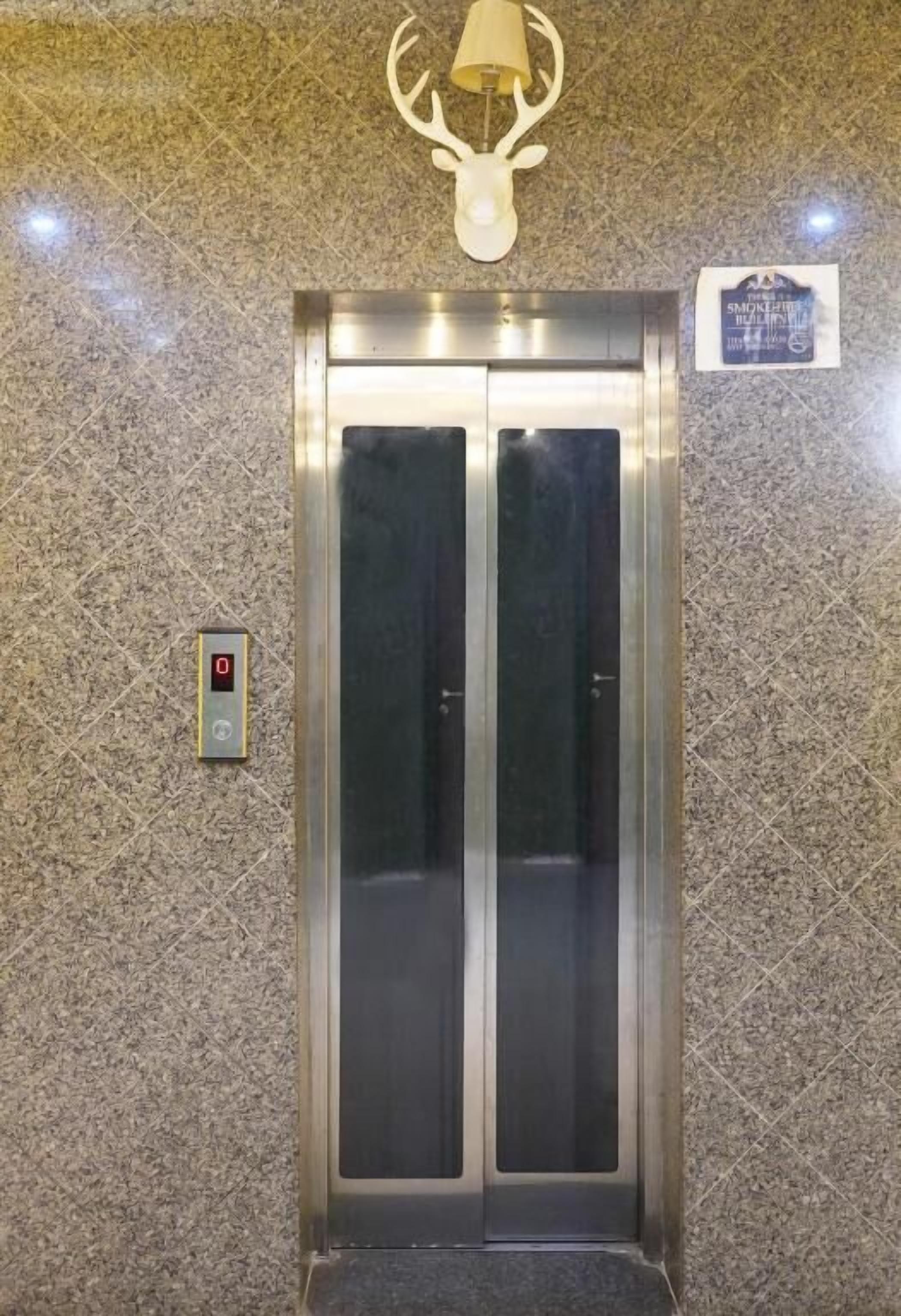 Een lift met een digitaal display, een decoratie van een hertenkop en een plaquette aan de muur.