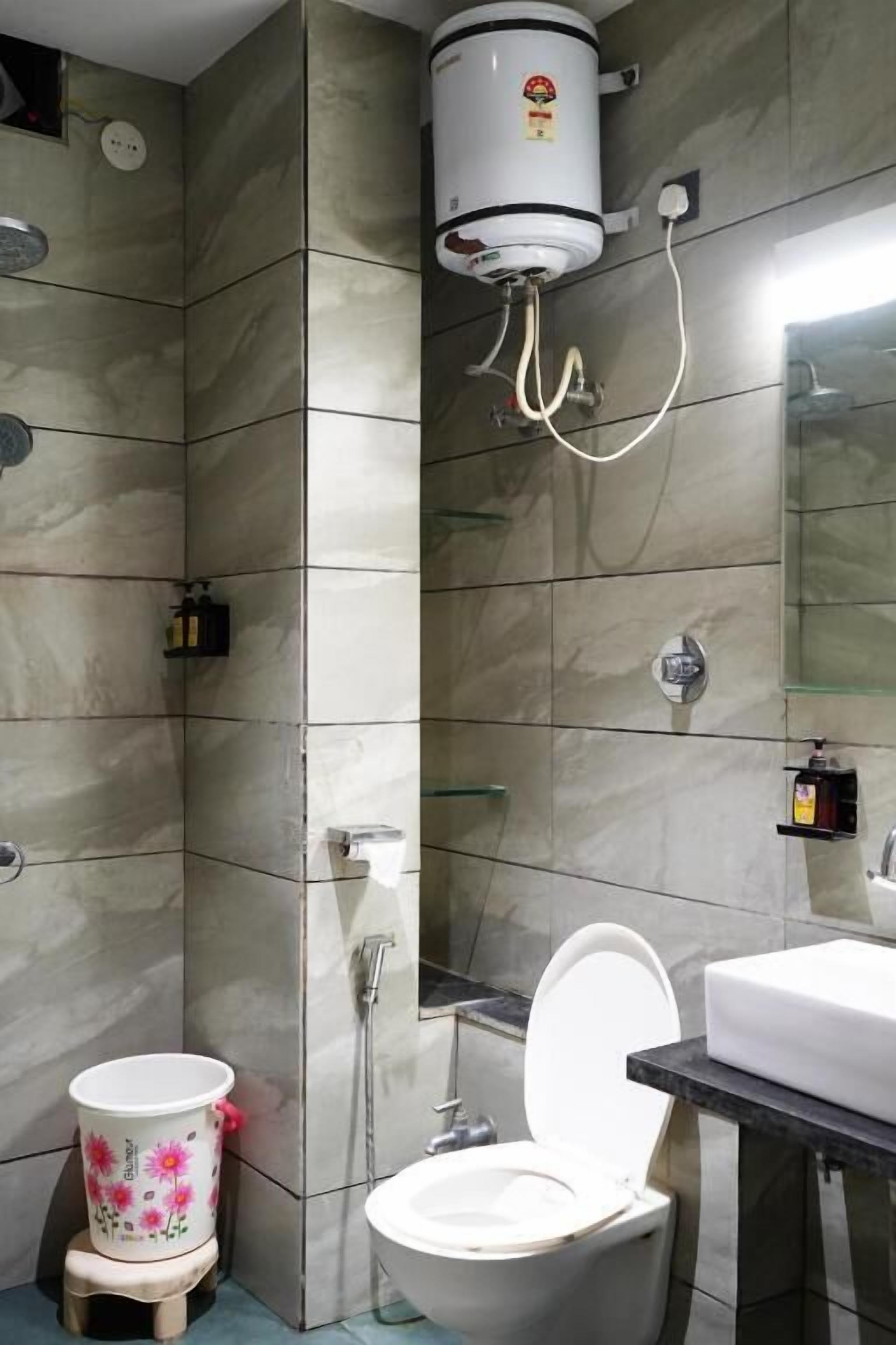 A bathroom with a toilet, a sink, a shower, and a water heater mounted on the wall.