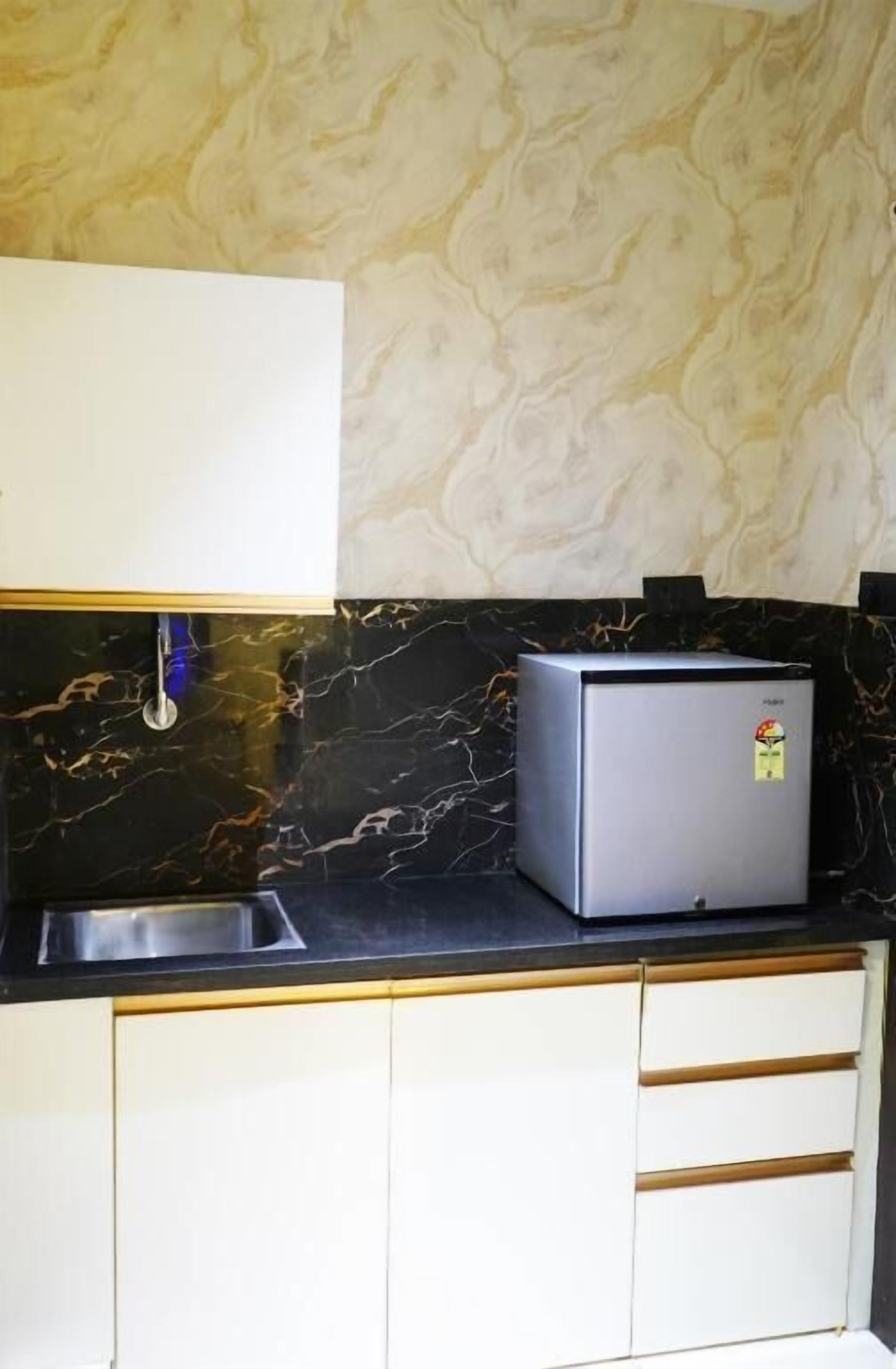 A kitchen with a marble backsplash, a stainless steel sink, and a refrigerator.