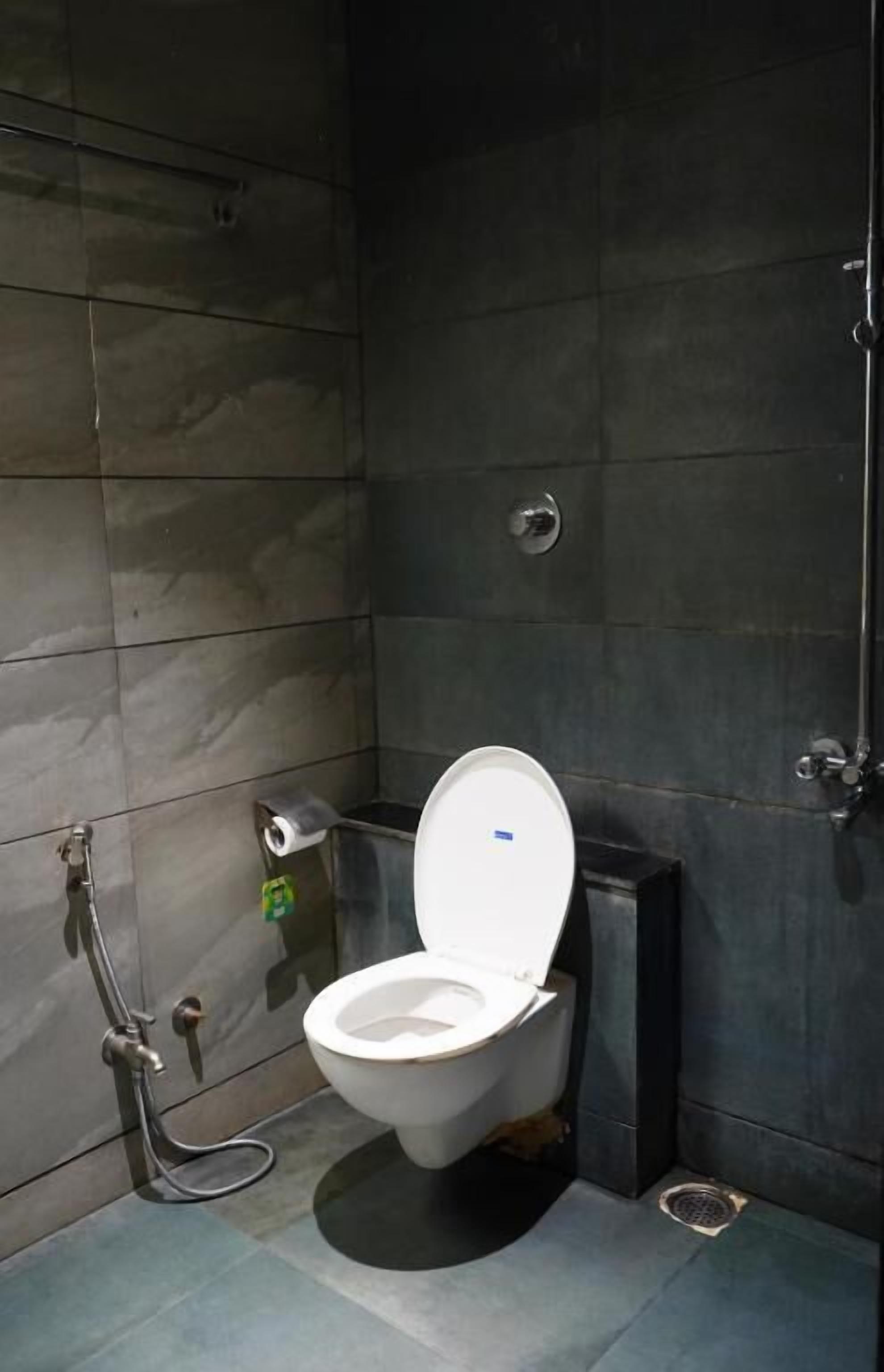 Et moderne badeværelse med toilet i hvidt, mørke flisevægge og et bruseområde.