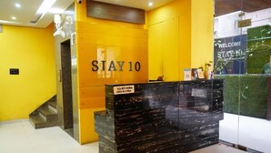 A reception desk with a 'STAY 10' sign, a glass partition, and a 'WELCOME STAY HOME' sign. - Stay10 Luxury Service Apartment (Indore)