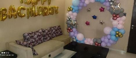 A room with a sofa, a wall decoration with balloons, and a table.