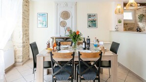 Een eetgedeelte met een houten tafel, zwarte stoelen en een witte wand met ingelijste foto's.