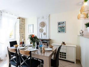 A dining area with a wooden table set for four, surrounded by chairs. There is a white cabinet with drawers to the right, and a wall-mounted shelf above the cabinet. - House in bastide, pets allowed - 5 guests (MONTFAUCON)