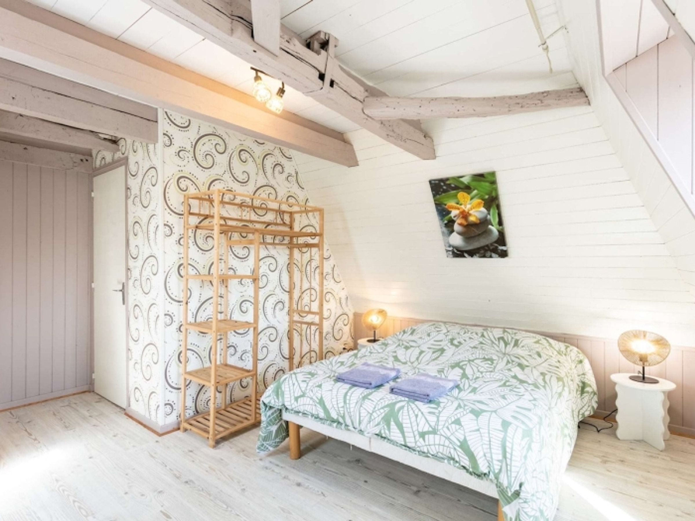 Un dormitorio con una cama, una escalera de madera, una pared con papel tapiz estampado y un cuadro en la pared.