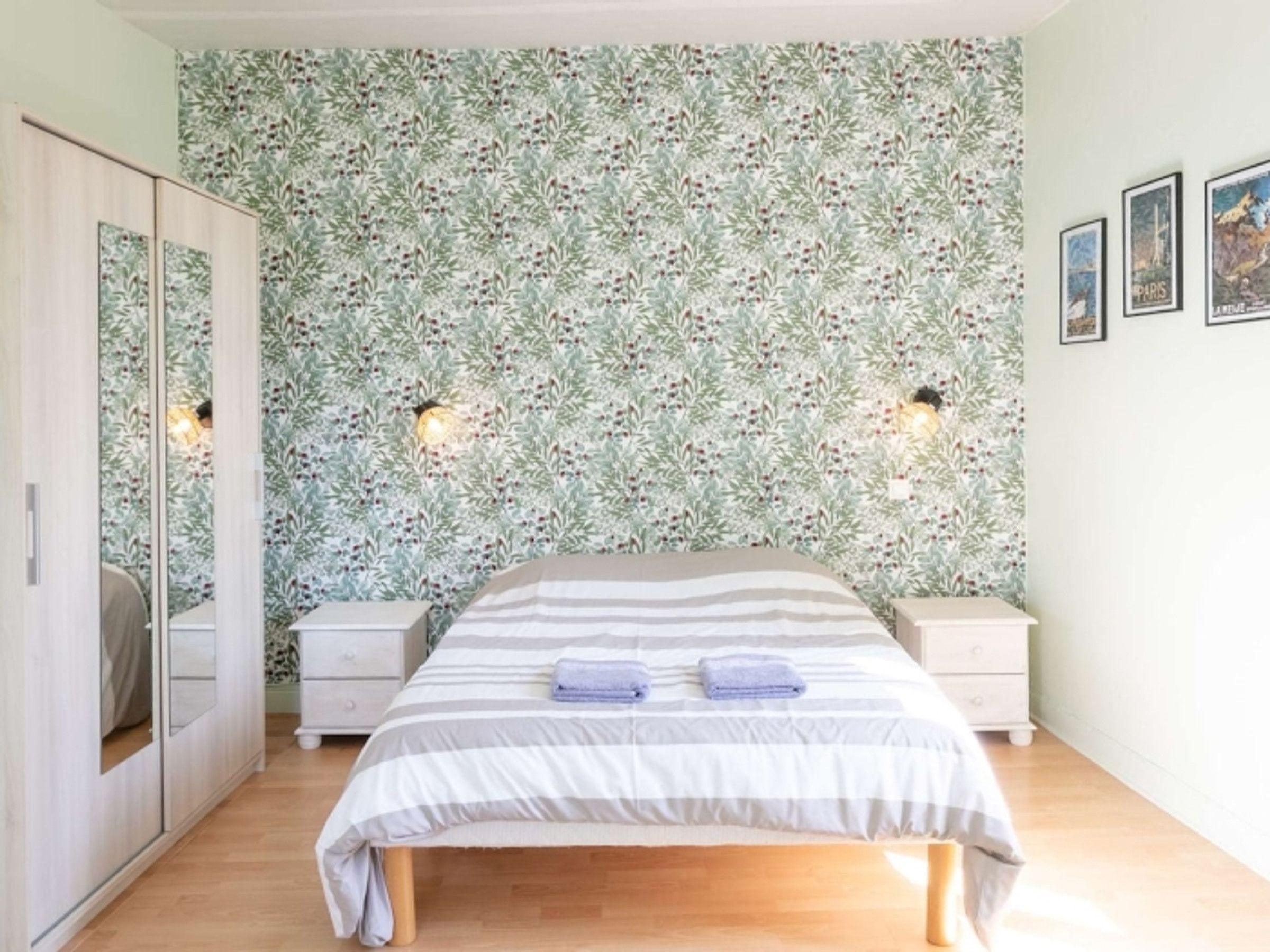 Een slaapkamer met een bed, nachtkastjes, een kledingkast en bloemenbehang.