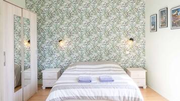 Een slaapkamer met een bed, nachtkastjes, een kledingkast en bloemenbehang.