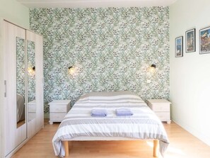 Ein Schlafzimmer mit Bett, Nachttischen, einem Kleiderschrank und blumigem Tapetenmuster.