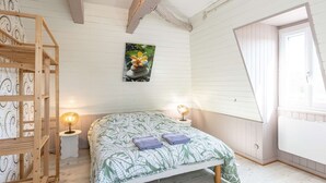 Een slaapkamer met een bed, een houten plank, een klein tafeltje met een lamp, een schilderij aan de muur en een raam.