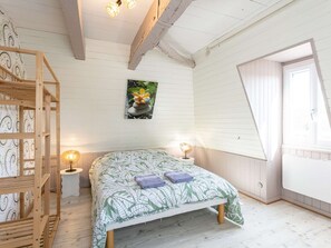 Une chambre à coucher avec un lit, une étagère en bois, une petite table avec une lampe, un tableau au mur et une fenêtre.