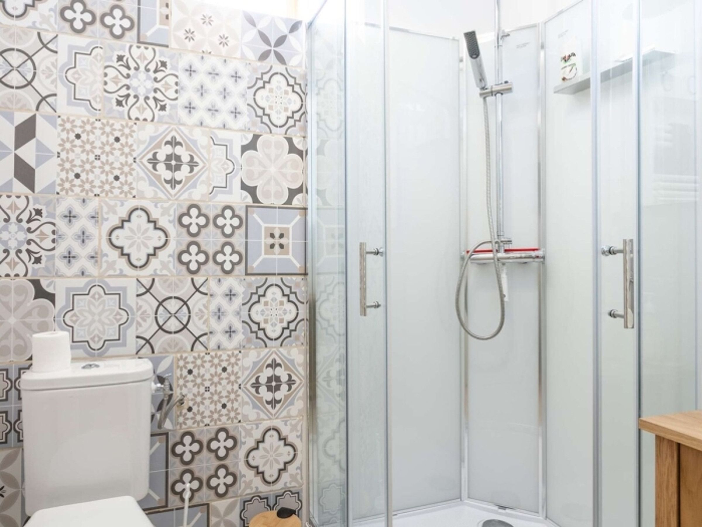 Une douche avec une porte en verre, des toilettes avec un rouleau de papier toilette et un mur décoré d’un motif.