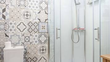 Une douche avec une porte en verre, des toilettes avec un rouleau de papier toilette et un mur décoré d’un motif.