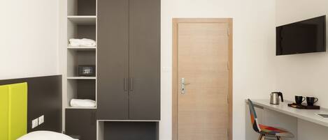 A hotel room with a bed, a wardrobe, a desk with a chair, a television, and a door.