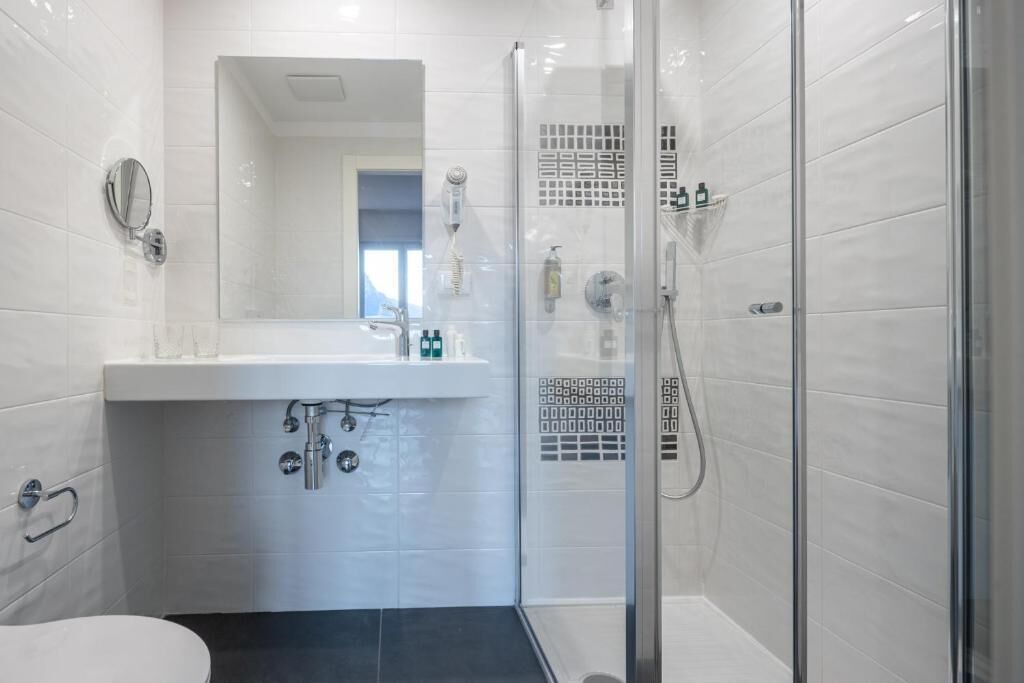 A modern bathroom with a glass shower enclosure, a white sink, and a mirror.