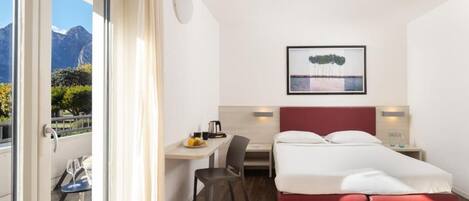 A hotel room with a bed, desk, chair, and a view of mountains through a window.