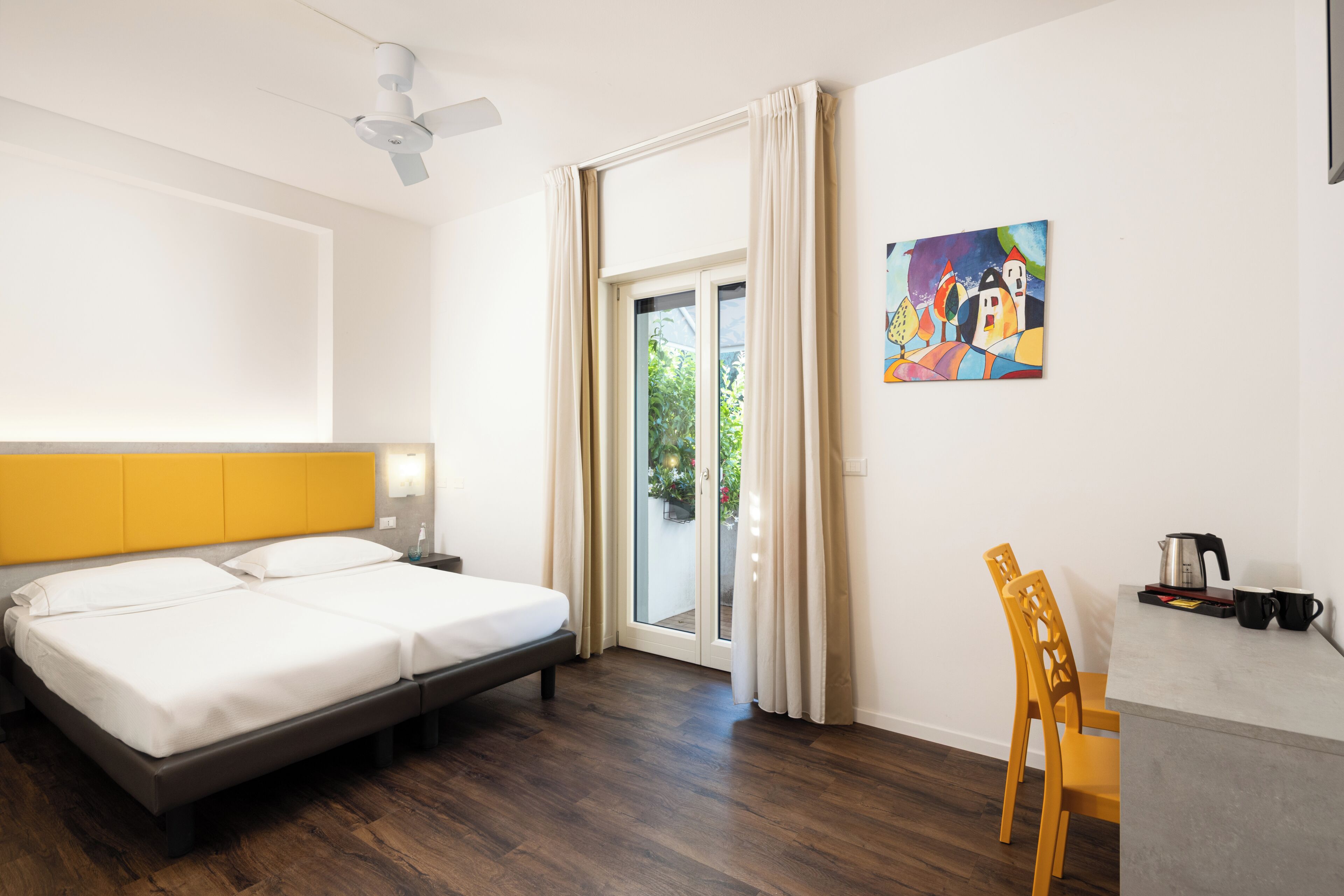 A hotel room with a bed, a desk, a chair, a painting, and a view through the window.