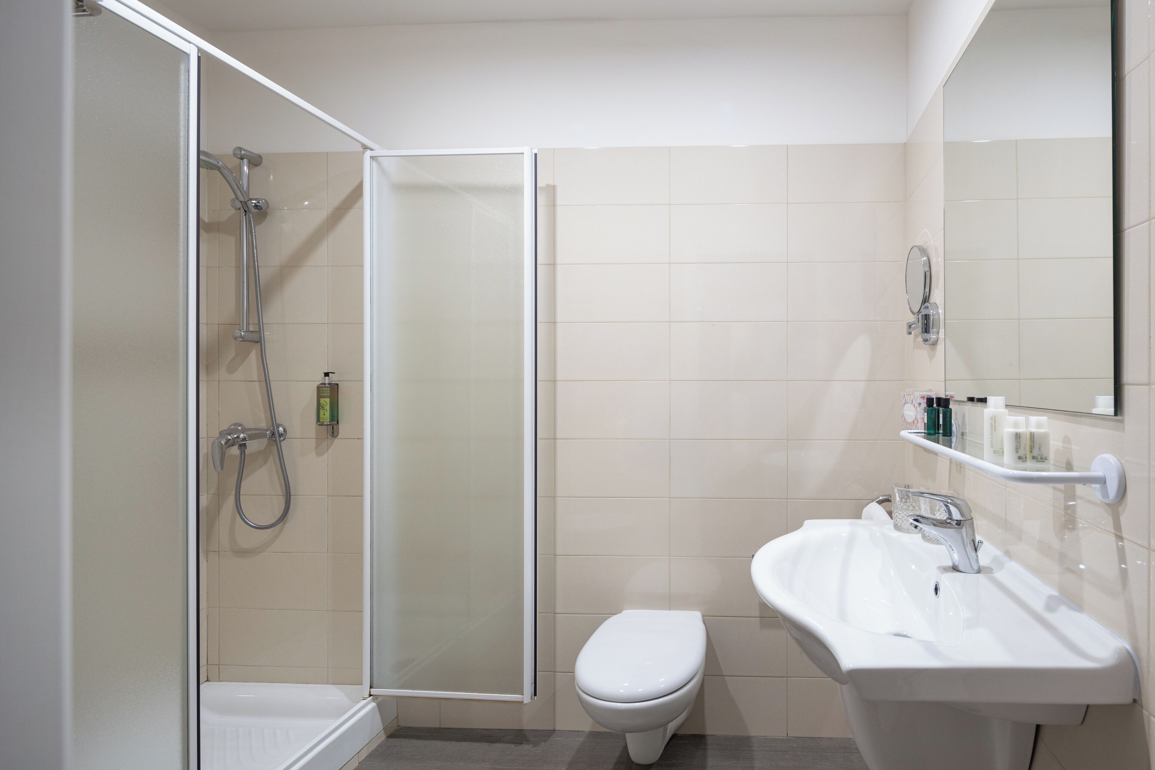A bathroom with a shower, toilet, sink, and mirror.