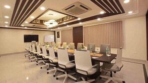 A conference room with a long table, multiple chairs, a flat-screen TV, and a ceiling with a geometric pattern. - Casa In Luxury Suites (Thiruvananthapuram)