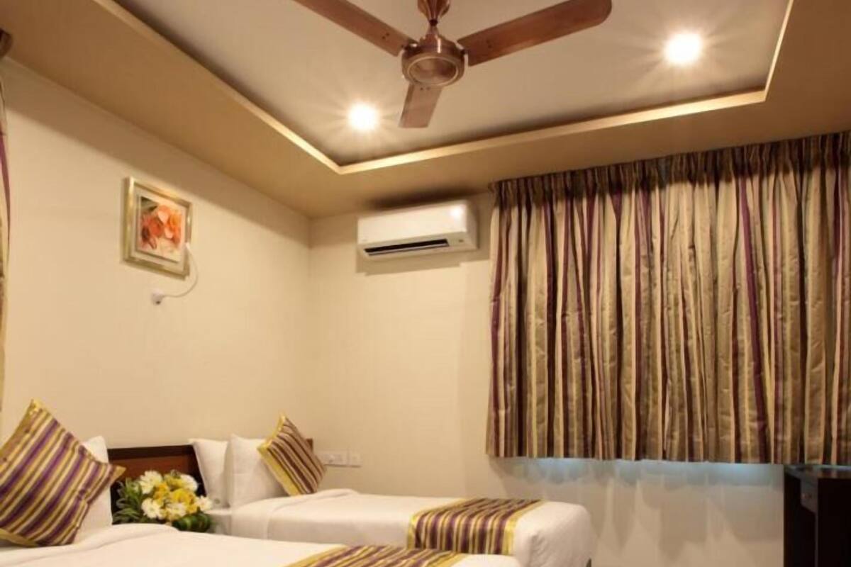 Habitación de hotel con dos camas, ventilador de techo, aire acondicionado y una ventana con cortinas.