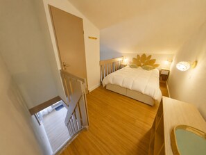 A bedroom with a wooden floor, a bed with a leaf-patterned headboard, a bedside table, and a nightstand with a lamp. - Apartment in Prémanon center - 6 guests (Prémanon)