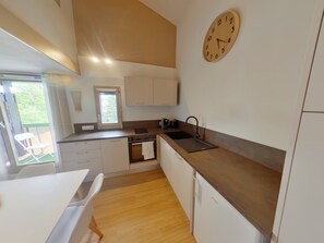 Eine moderne Küche mit Holzboden, weißen Schränken, einem eingebauten Ofen, einer Spüle und einer Uhr an der Wand.