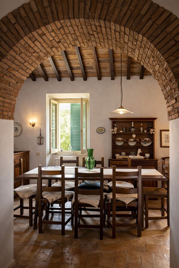 A rustic dining area with a brick arch, wooden table, chairs, and a hanging light fixture.