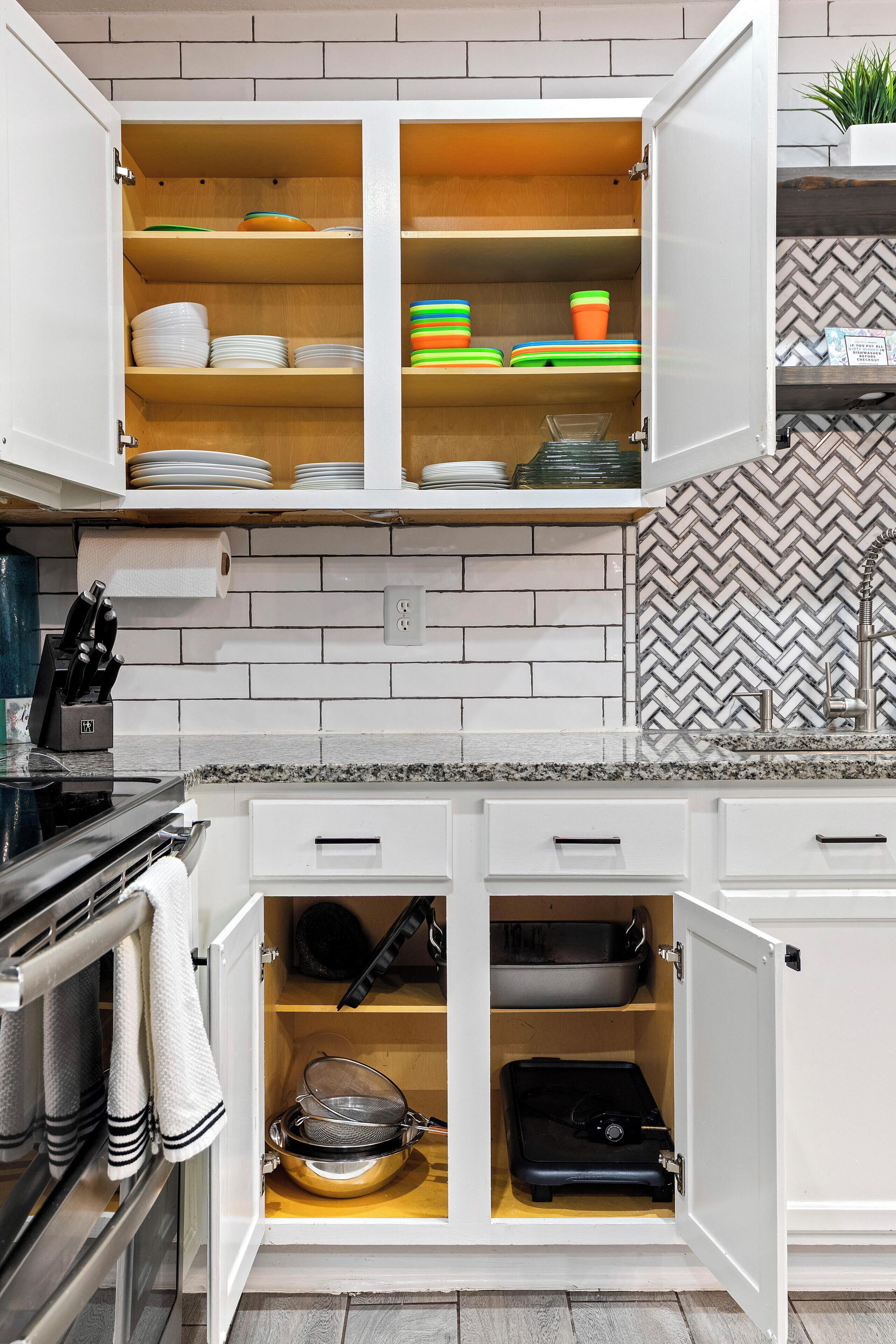 A kitchen with open cabinets containing dishes, a strainer, and a suitcase.