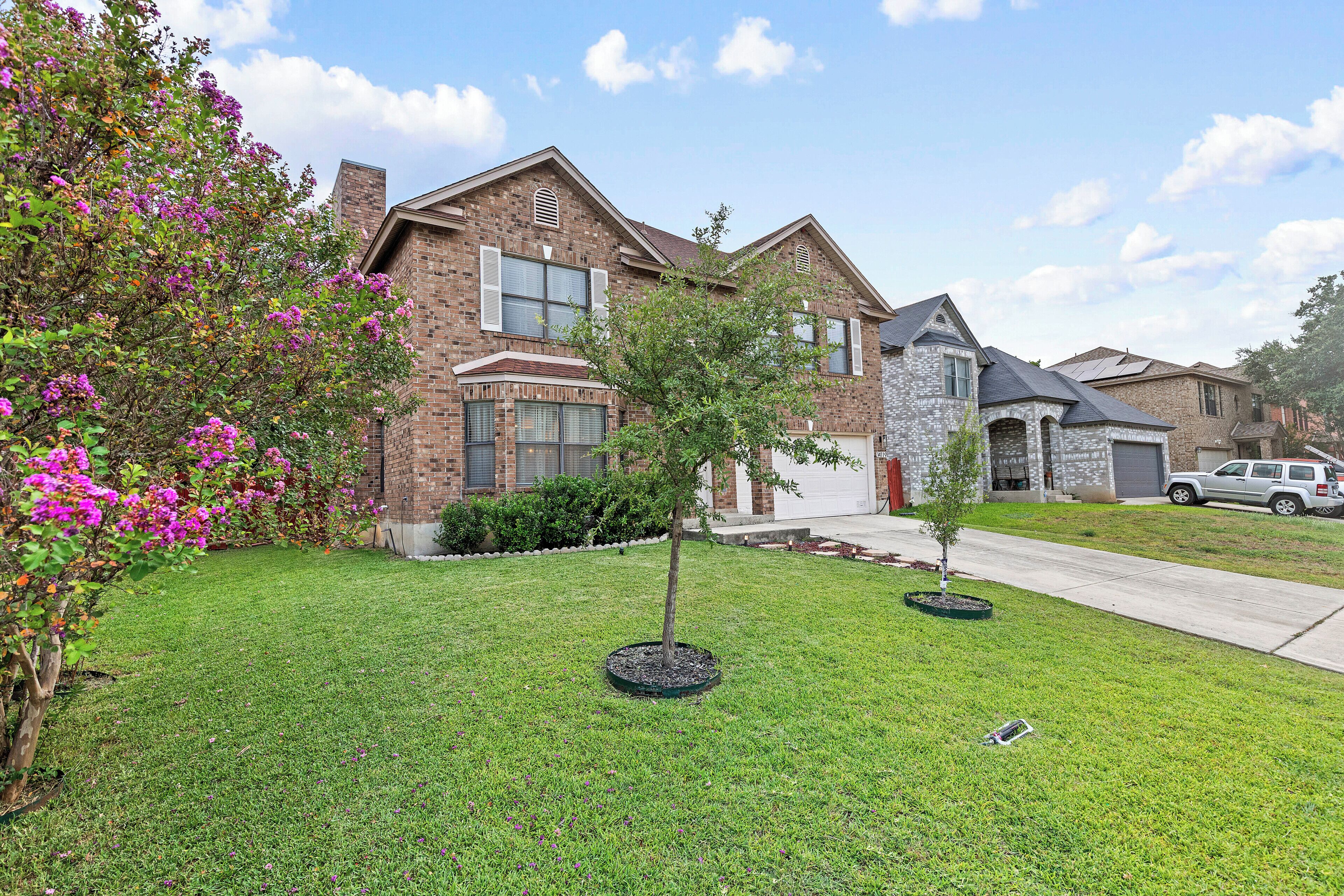 A residential house with a brick facade, a well-maintained lawn, and a small tree in the front yard.