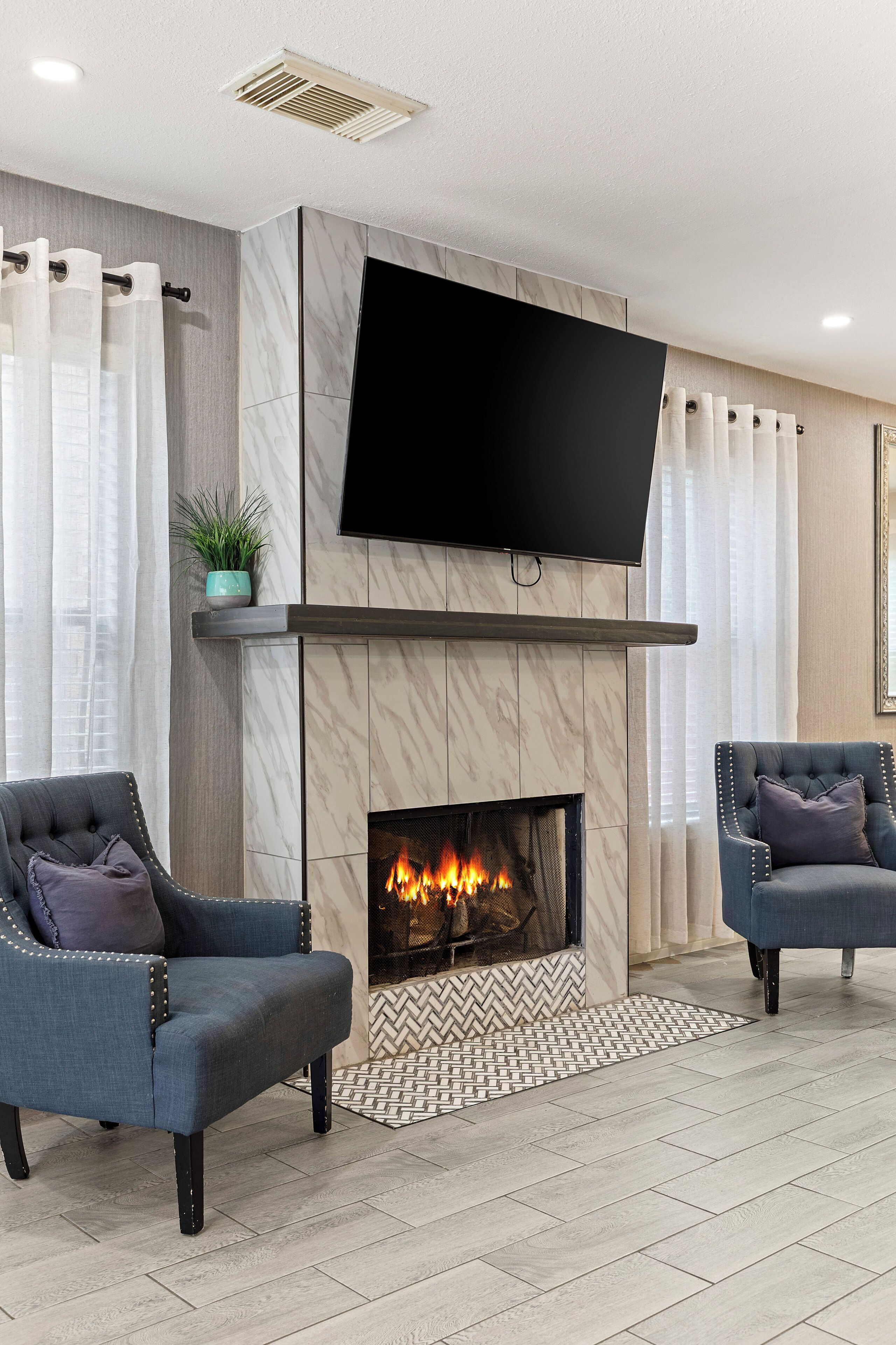 A modern living room with a fireplace, two armchairs, a flat-screen TV, and a potted plant.