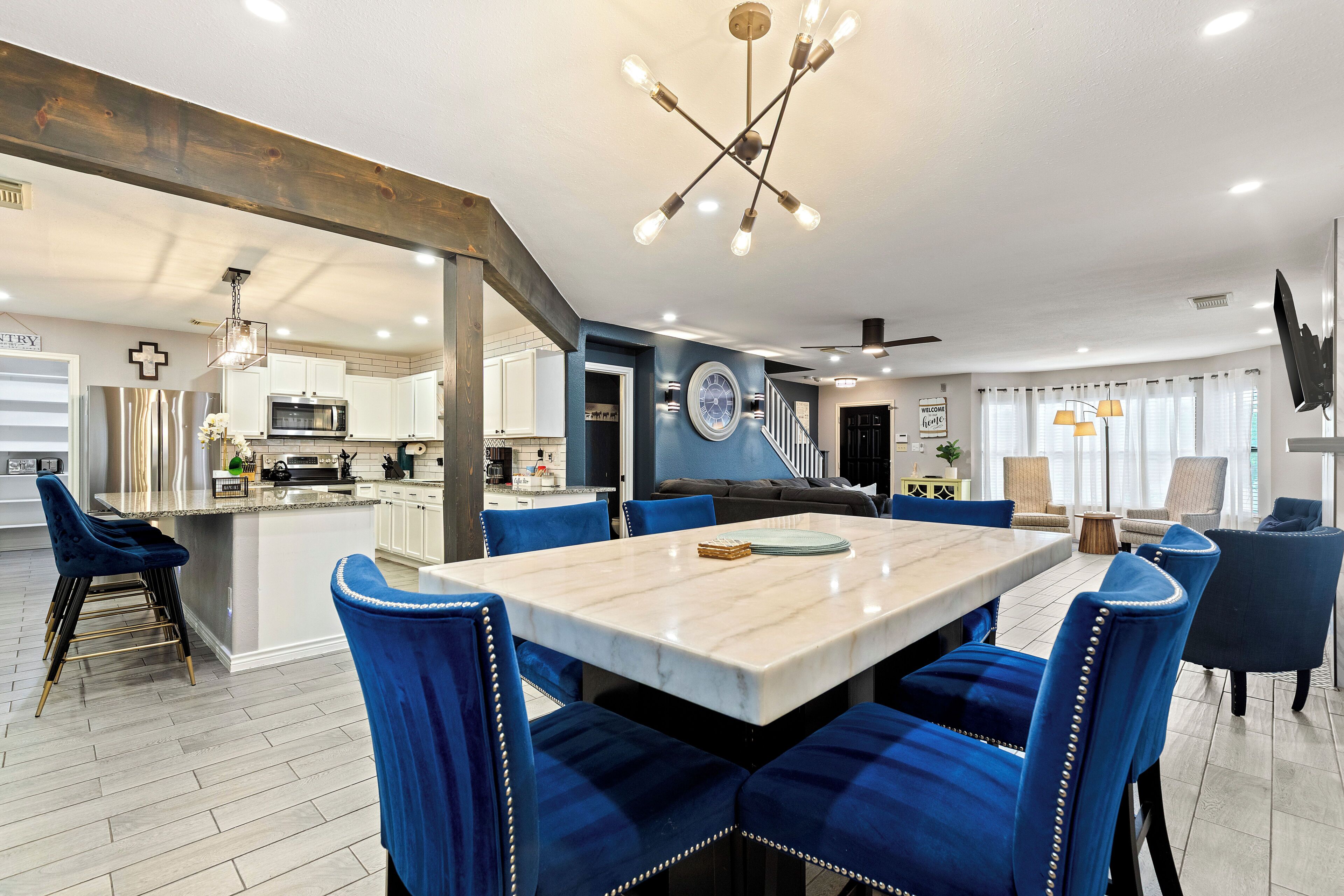 A modern kitchen with stainless steel appliances, a dining area with blue upholstered chairs, and a large island.