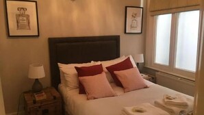 Ein ordentlich gemachtes Bett mit Kissen, eine Nachttischlampe, ein Nachttisch mit Lampe und gerahmte Bilder an der Wand.