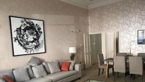 Ein modernes Wohnzimmer mit einem grauen Sofa, einem Glastisch, einem Essbereich mit Tisch und Stühlen sowie einem großen abstrakten Gemälde an der Wand.