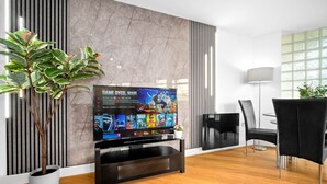 A modern living room with a flat-screen TV, a dining area with black chairs, a potted plant, and a marble wall. - City Centre Apartment - Balcony - On Street Parking - Smart Tv & Neflix (Birmingham)