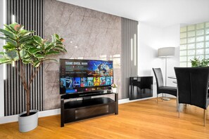 Ein modernes Wohnzimmer mit Flachbildfernseher, einem Essbereich mit schwarzen Stühlen, einer Topfpflanze und einer Marmorwand.