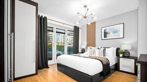A modern bedroom with a large bed, a bedside table with a lamp, a framed picture on the wall, and a view through the window. - City Centre Apartment - Balcony - On Street Parking - Smart Tv & Neflix (Birmingham)