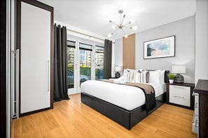 Ein modernes Schlafzimmer mit einem großen Bett, einem Nachttisch mit Lampe, einem gerahmten Bild an der Wand und Blick aus dem Fenster.