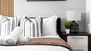 A neatly made bed with striped bedding, a bedside lamp, a small potted plant, and a framed picture on the wall. - City Centre Apartment - Balcony - On Street Parking - Smart Tv & Neflix (Birmingham)