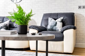 A modern living room with a sofa, a round coffee table, and a potted plant. - City Centre Apartment - Balcony - On Street Parking - Smart Tv & Neflix (Birmingham)