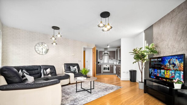 A modern living room with a sofa, coffee table, and TV, a kitchen in the background, and a brick wall. - City Centre Apartment - Balcony - On Street Parking - Smart Tv & Neflix (Birmingham)