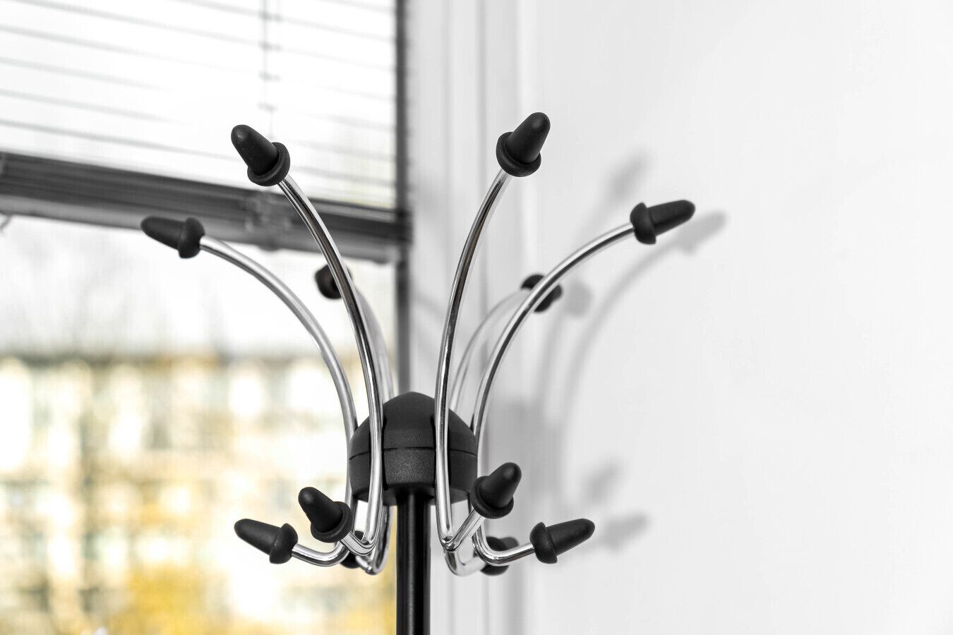 A black metal coat rack with multiple hooks against a white wall, with a window in the background.