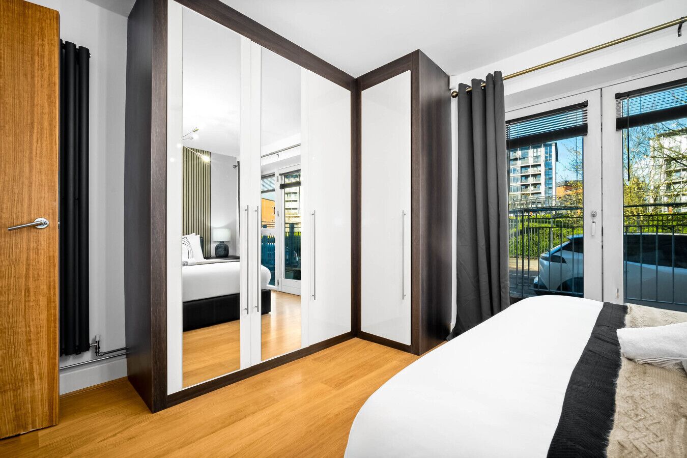 A bedroom with a bed, a wardrobe, a mirror, and a view of the outside.