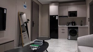 Una moderna camera d'hotel con TV a schermo piatto, un ampio specchio, un tavolo da pranzo, un divano e un angolo cottura completo di forno a microonde, frigorifero e lavatrice.