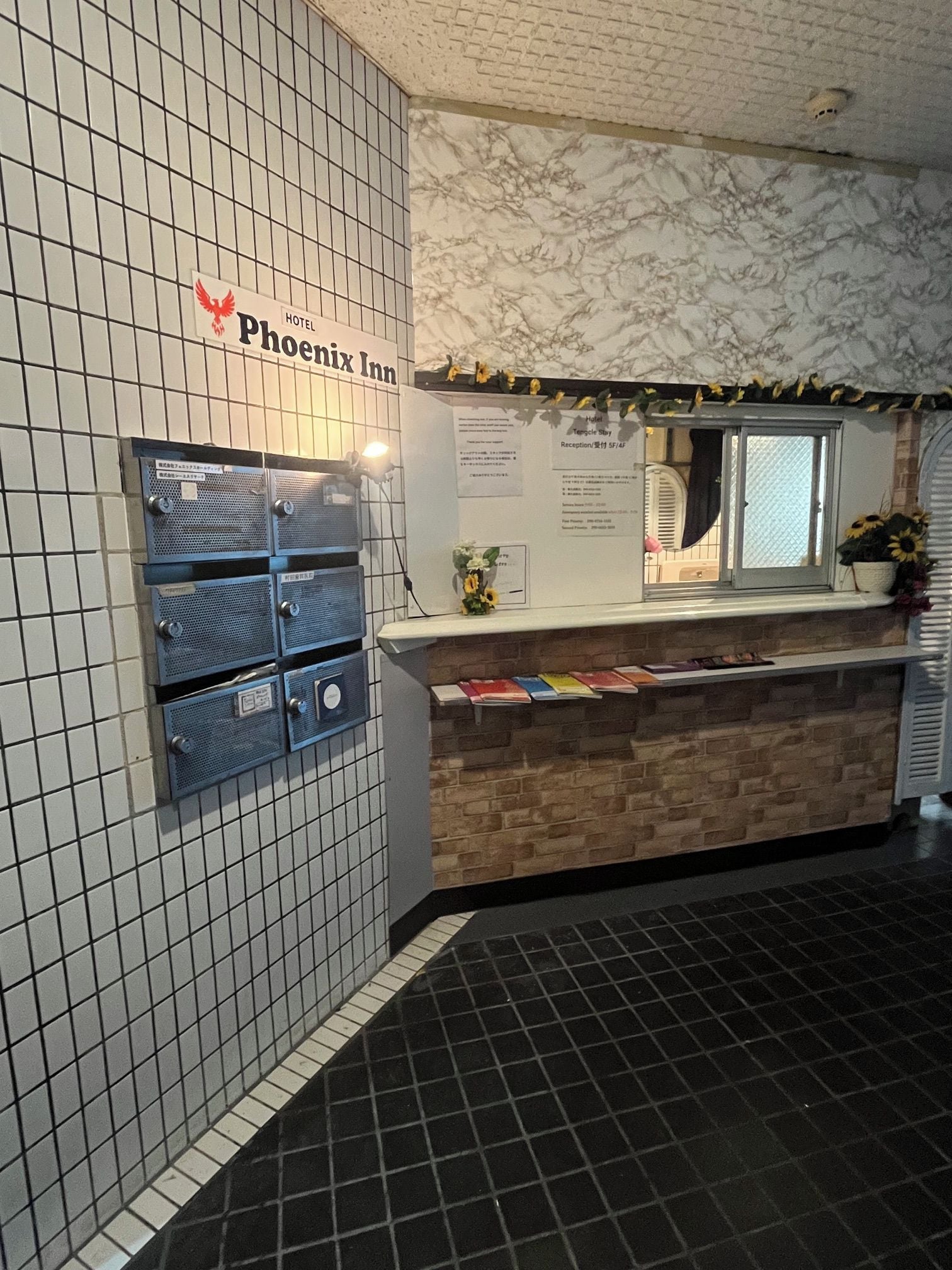 A hotel reception area with a tiled wall, a reception desk with a flower vase, and a sign for the Phoenix Inn.