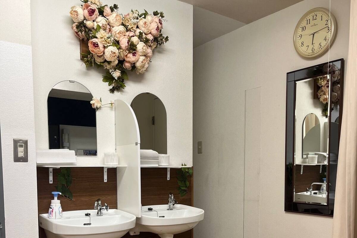 A bathroom with two sinks, a clock, and a floral arrangement.